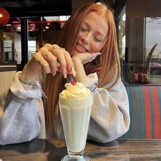 a woman sitting at a table with a milkshake and whip cream in front of her