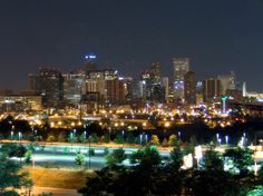 the city is lit up at night with lights on and trees in front of it