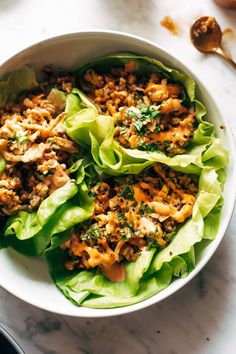 a white bowl filled with lettuce covered in meat and seasoning sitting on top of a marble counter