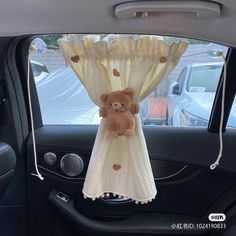 a stuffed teddy bear hanging from the back of a car window in front of a curtain