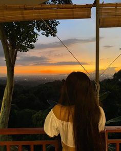 a woman sitting on a bench looking out over the city at sunset with her long hair blowing in the wind