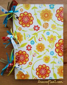 an open book with colorful flowers and ribbons on the cover is sitting on a wooden table