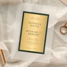 a wedding card with two gold rings on it next to a pen and ring holder