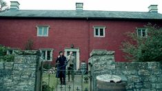 two people standing in front of a red brick building with an iron fence and gate