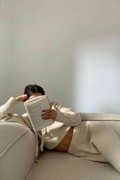 a woman laying on a couch reading a book