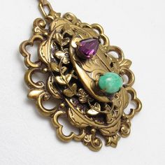 Large vintage rhinestone pendant is stunning in gold tone metal.   A green marbled glass stone and purple marquis rhinestone are prong set on the top of a stacked design.  Fleur de lis design is on the the side of the bottom layer.  On the second layter a vine of leaves surround it.  A unique beautiful vintage pendant.  I added a vintage Monet twisted serpentine chain so it is ready to wear.  Unmarked  beauty.  Pendant measures 1 7/8 X 1 5/8 inches and chain is about 23 1/2 inches long with a sp Ornate Jeweled Pendant Jewelry, Vintage Oval Jeweled Necklaces, Vintage Jeweled Oval Necklace, Vintage Oval Jeweled Necklace, Green Vintage Charm Pendant Jewelry, Green Pendant Jewelry With Vintage Charm, Antique Jeweled Metal Jewelry, Jeweled Antique Gold Brass Jewelry, Victorian Brass Jewelry With Large Pendant