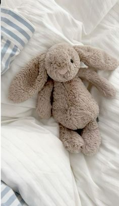 a stuffed animal sitting on top of a bed under a white comforter with blue striped pillows