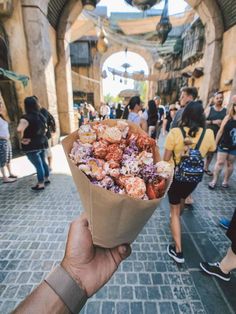 a hand holding up a paper bag filled with lots of food on top of a street