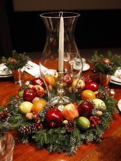 a table topped with a centerpiece filled with fruit and greenery next to a candle