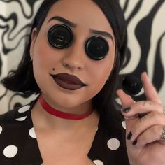 a woman with fake eyes and black lipstick holding up her finger to the camera while wearing a polka dot shirt