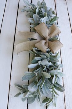 a wreath with green leaves and a bow on top of white wood planked floor