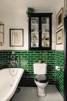 a white toilet sitting next to a bath tub in a bathroom with green tiles on the walls