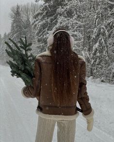 a woman walking down a snow covered road holding a christmas tree in her hand,