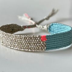 a blue and silver bracelet with red beads on it's end, sitting on a white surface