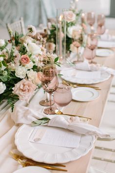 the table is set with white and gold plates, silverware, and pink flowers