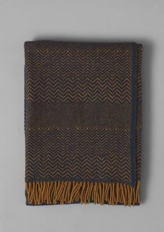 a brown and black herringbone throw with fringes on it's end, against a gray background