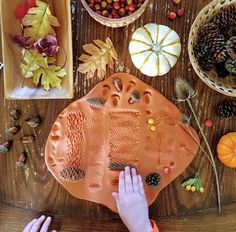 a child's hand on a clay plate surrounded by fall leaves and acorns