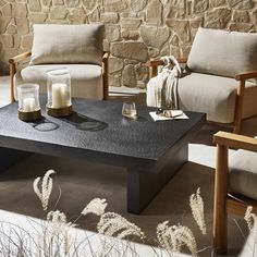 two chairs and a coffee table in front of a stone wall with candles on it