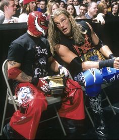 two men in wrestling gear sitting next to each other on a bench with people behind them