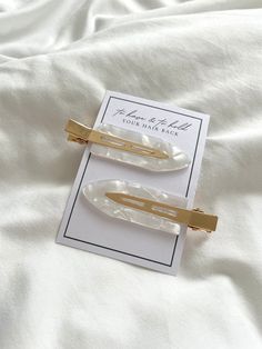 two hair clips sitting on top of a white sheet covered bed next to each other