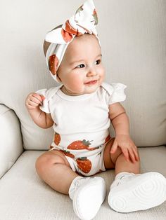 a baby sitting on a couch wearing a white outfit with strawberrys on it's head