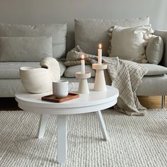 a white coffee table with two candles on it in front of a gray couch and pillows