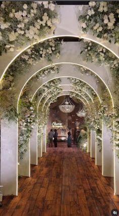 an archway decorated with white flowers and greenery is lit up by led lights at the end