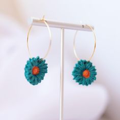 a pair of blue and orange flowers are hanging from hoop earrings on a white stand