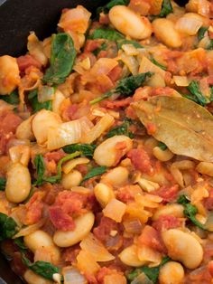 a skillet filled with pasta and spinach covered in tomato sauce next to a wooden spoon