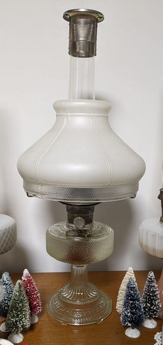 a white lamp sitting on top of a wooden table next to small christmas trees and other decorations