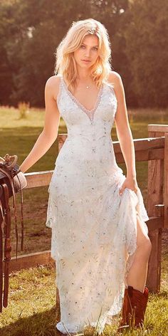 a beautiful blonde woman in a white dress sitting on a fence next to a horse