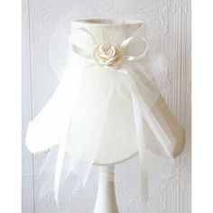 a white lamp shade with a flower on the top and a ribbon around it's neck