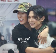 two young men hugging each other in front of microphones and an advertisement behind them