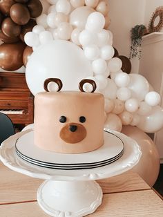 a cake on a plate with balloons in the background and a teddy bear head on top