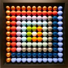 an art work made out of different colored balls in a square frame on the wall