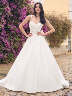 a woman in a white wedding dress standing on a cobblestone road with her hands on her hips