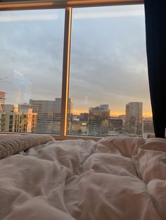 a bed in front of a large window with cityscape outside it and the sun setting