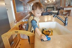 a young boy playing with toy cars in his kitchen sink and countertop area at home