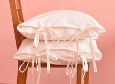 two white pillows tied together on top of a wooden chair in front of a pink wall