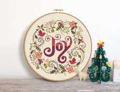 a cross stitch christmas ornament with the word joy on it next to a small tree