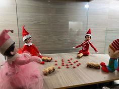 three elfs sitting at a table with food and candy in front of them,