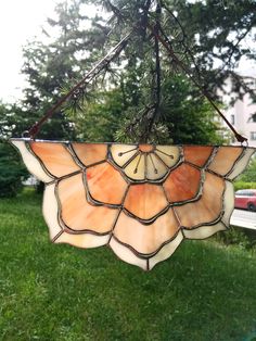 a stained glass sun catcher hanging from a tree in the grass with a house in the background