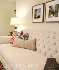 a living room with white couches and pictures on the wall above them in front of a lamp