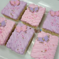 six decorated cookies with pink frosting and purple icing on a white platter