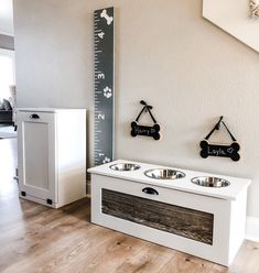 a white dog house with two bowls and a ruler on the wall next to it