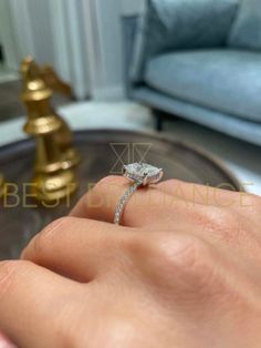 a woman's hand with a diamond ring on it, in front of a couch