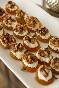 small appetizers are arranged on a white platter with walnuts and goat cheese