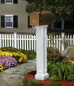 a white post with a mailbox on it in front of a fence and flowers