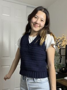 a woman standing in front of a white door wearing a blue knitted sweater vest