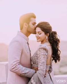 a man and woman standing next to each other in front of the sun with their faces close together